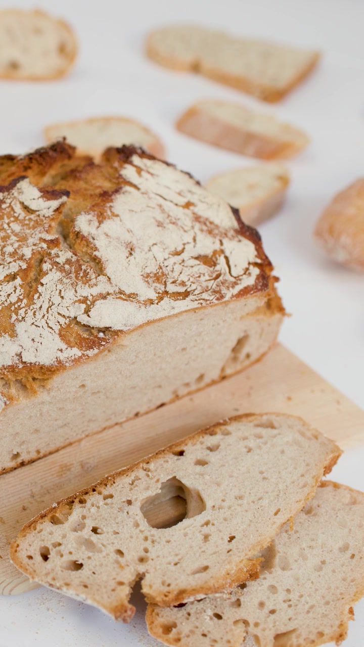 Person picks up fresh sourdough slice from wooden board against bright white background studio lighting.