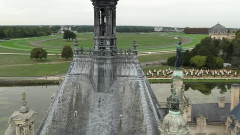 aerial view of chateau de chantilly rooftop tower with racecourse beyond, france. historic french castle, landmark, equestrian estate, travel