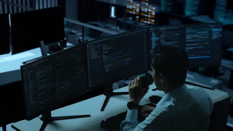 vista lateral de un desarrollador asiático bebiendo café y usando una computadora para escribir código con múltiples pantallas en la oficina