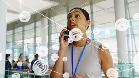 Animation-of-connected-icons-with-lines-over-biracial-woman-talking-on-cellphone-at-office