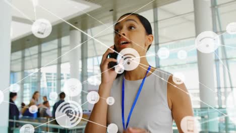 animation of connected icons with lines over biracial woman talking on cellphone at office