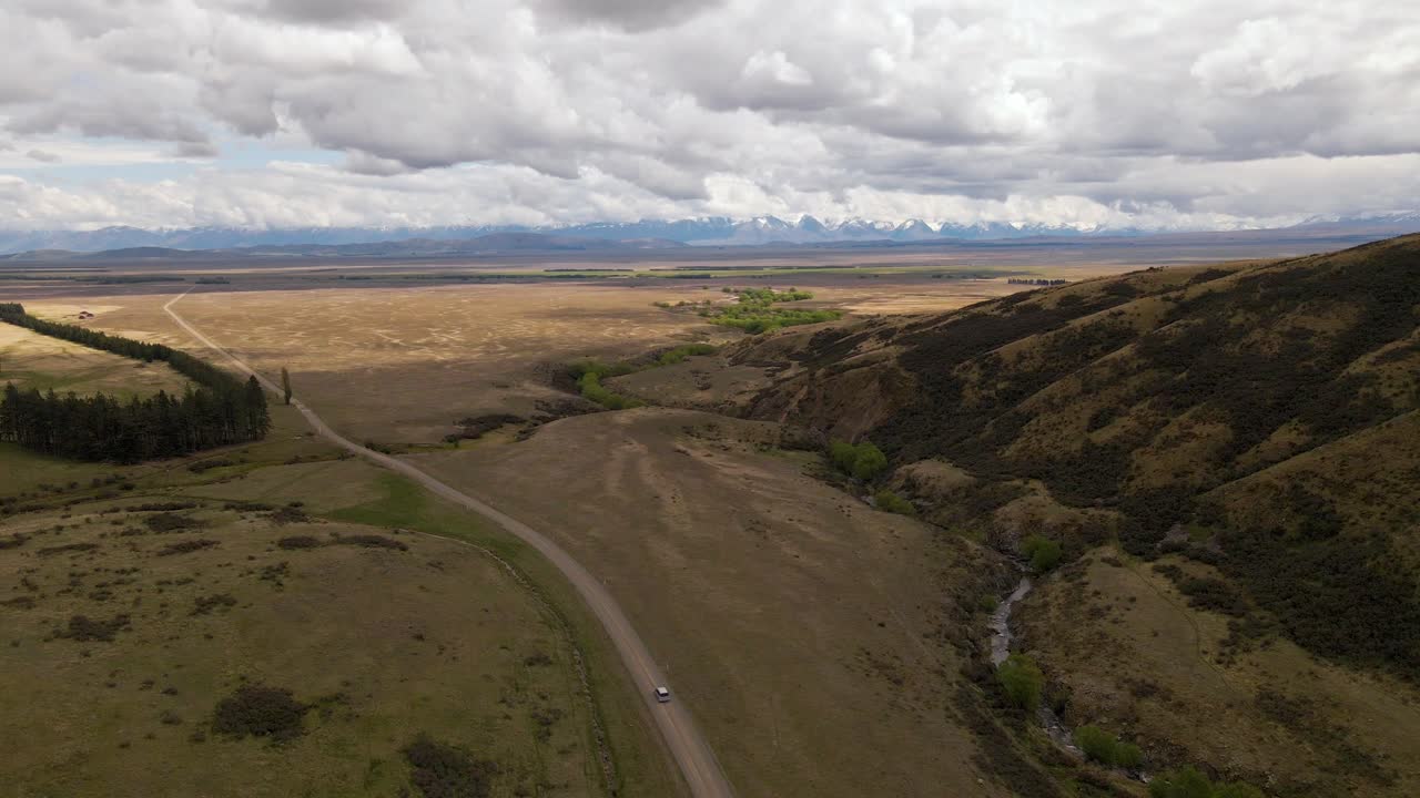 antena de alto ángulo siguiendo el coche que conduce por un camino de tierra dentro de un paisaje montañoso seco