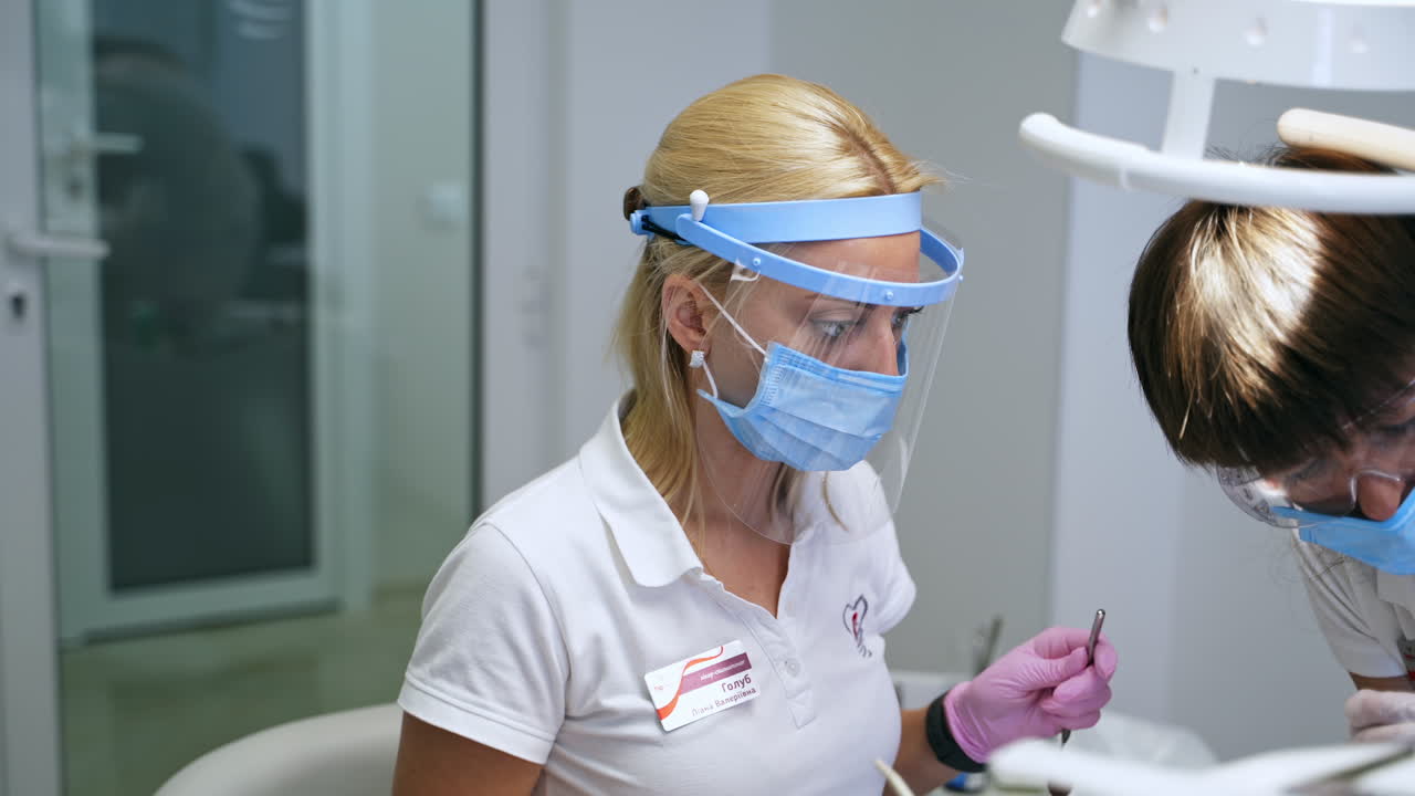Female blonde doctor wearing mask and protective shield. Doctor working in the dental clinics.