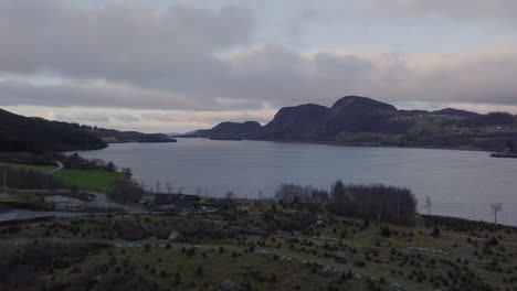 Drone-flyover-christmas-tree-plantation-to-scenic-lakeside,-Norway-rural-area,-moody-cloudy-day