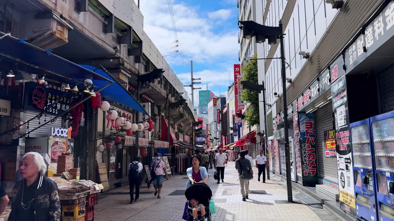 Bustling pedestrian street in Japan with shops, bright signs, and people walking under a blue sky