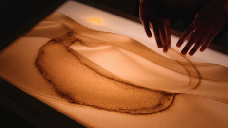 hands interacting with an illuminated sand art table