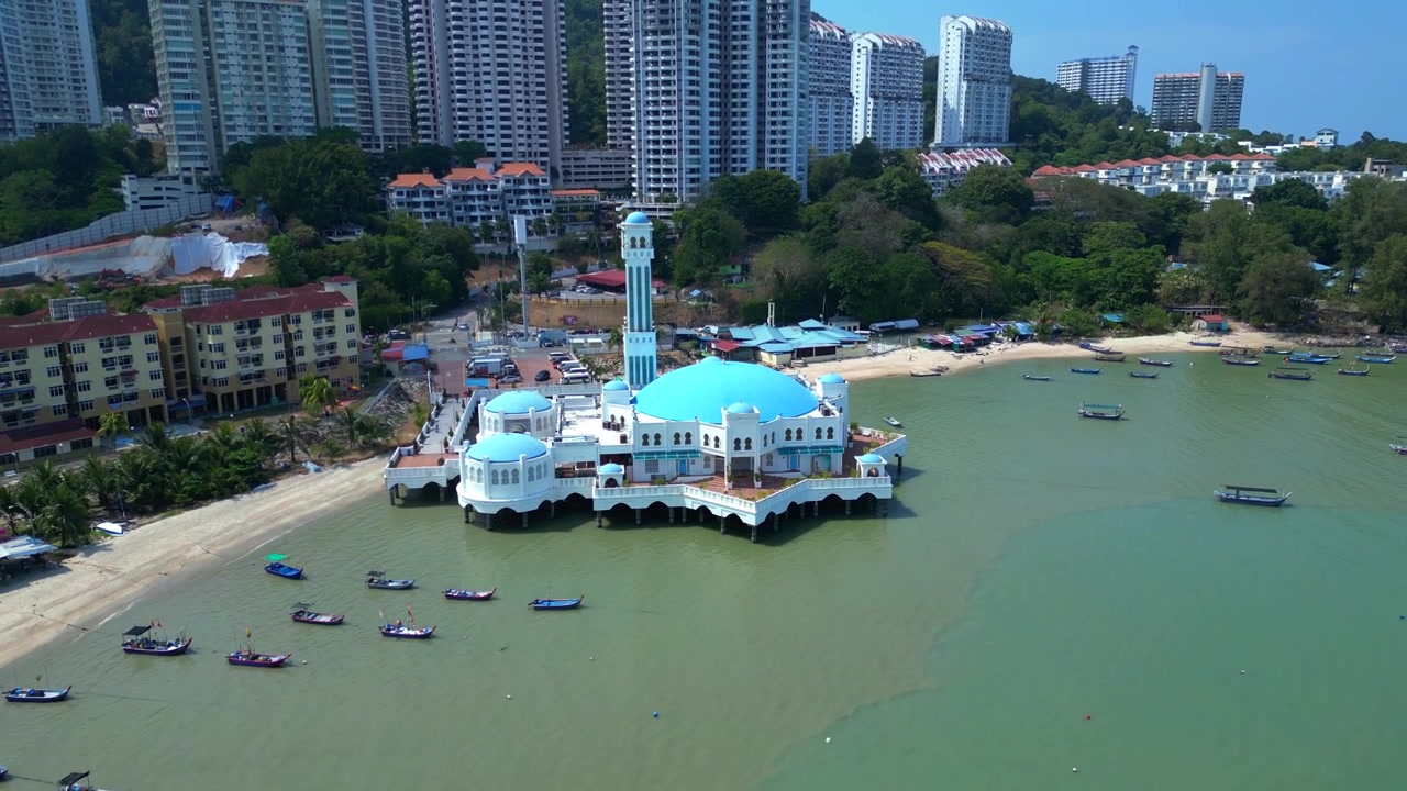 Masjid Sultan Ahmad Shah mengapung di atas air dengan perahu dan gedung apartemen di sekitarnya di Tanjung Bungah, Penang. Pemandangan udara mulus yang naik ke atas dengan panorama drone