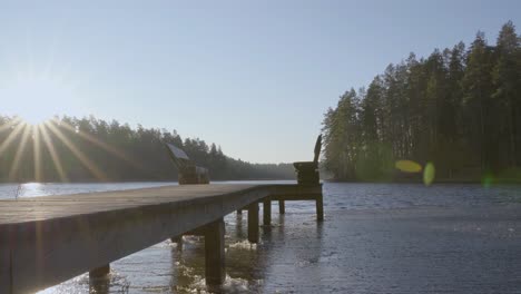 empty wooden benches at end of wooden pier beside calm lake amidst tall trees during sunrise