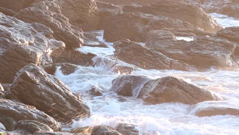 the sun rises over the horizon, illuminating the sea as waves crash against the rocks