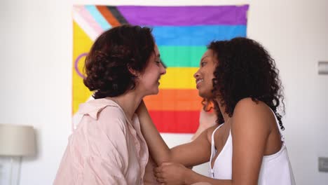 Happy-diverse-lesbian-couple-sitting-together-against-rainbow-flag