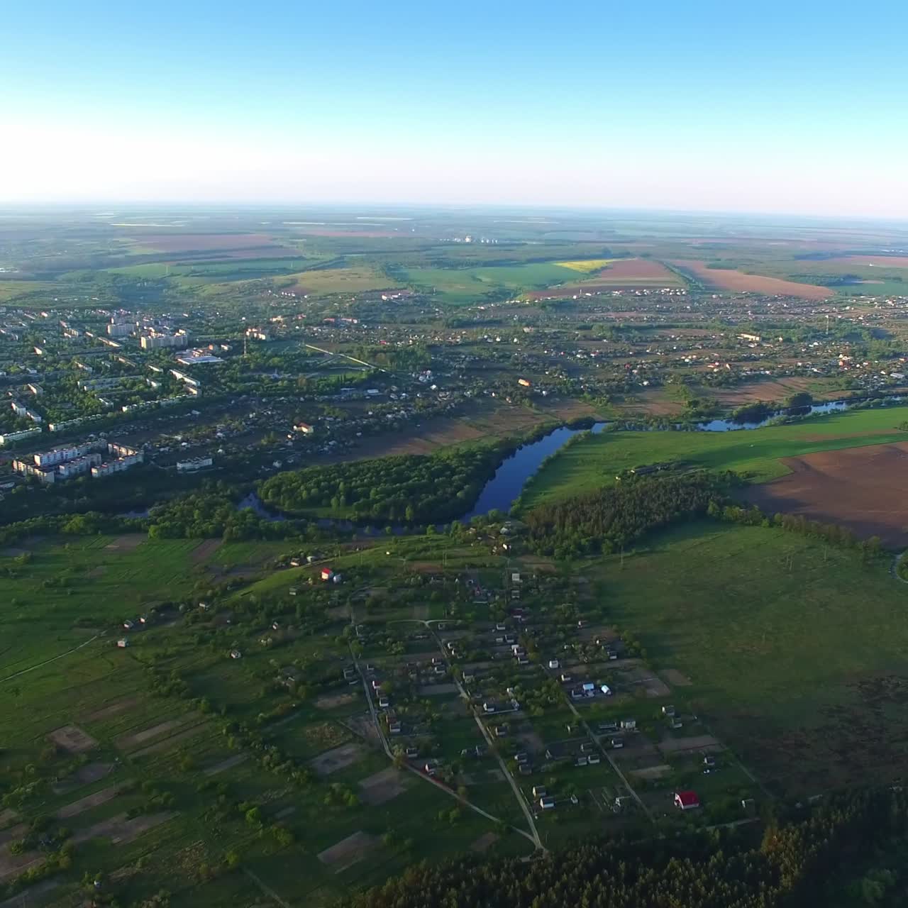 Vast scenic view of urban area and suburbs on sunny day. Wavy river crossing the green landscape. City dwelling around water artery. Top view