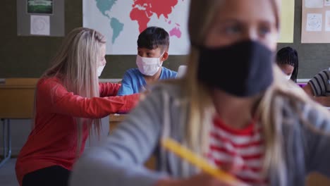 female teacher and boy wearing face mask using laptop in class at school