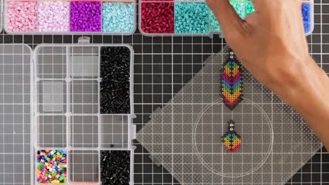 Colorful-fusion-beads-craft-on-pegboard,-hand-placing-beads,-creative-hobby,-Overhead-view-timelapse