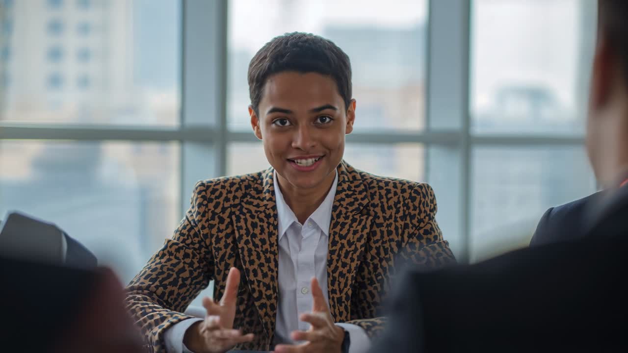Answering panel question, candidate speaking, leaning and gesturing at office table, leopard blazer