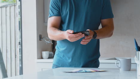 Hombre-Renovando-La-Cocina-En-Casa-Tomando-Fotografías-De-Muestras-De-Colores-De-Pintura-En-El-Teléfono-Móvil.