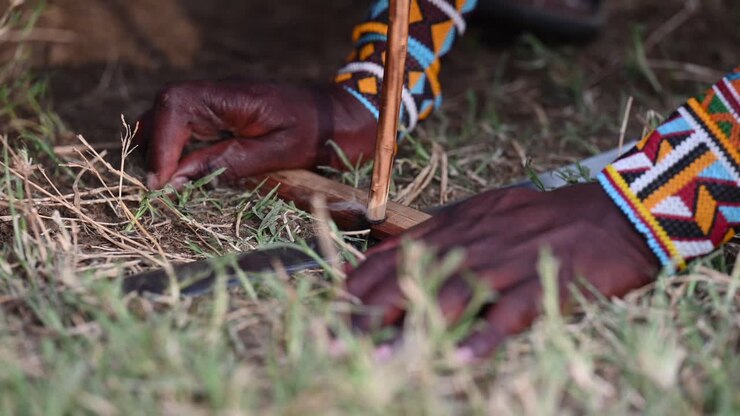 Maasai men are using the bow drill technique to start a fire at the Maasai village in Kenya