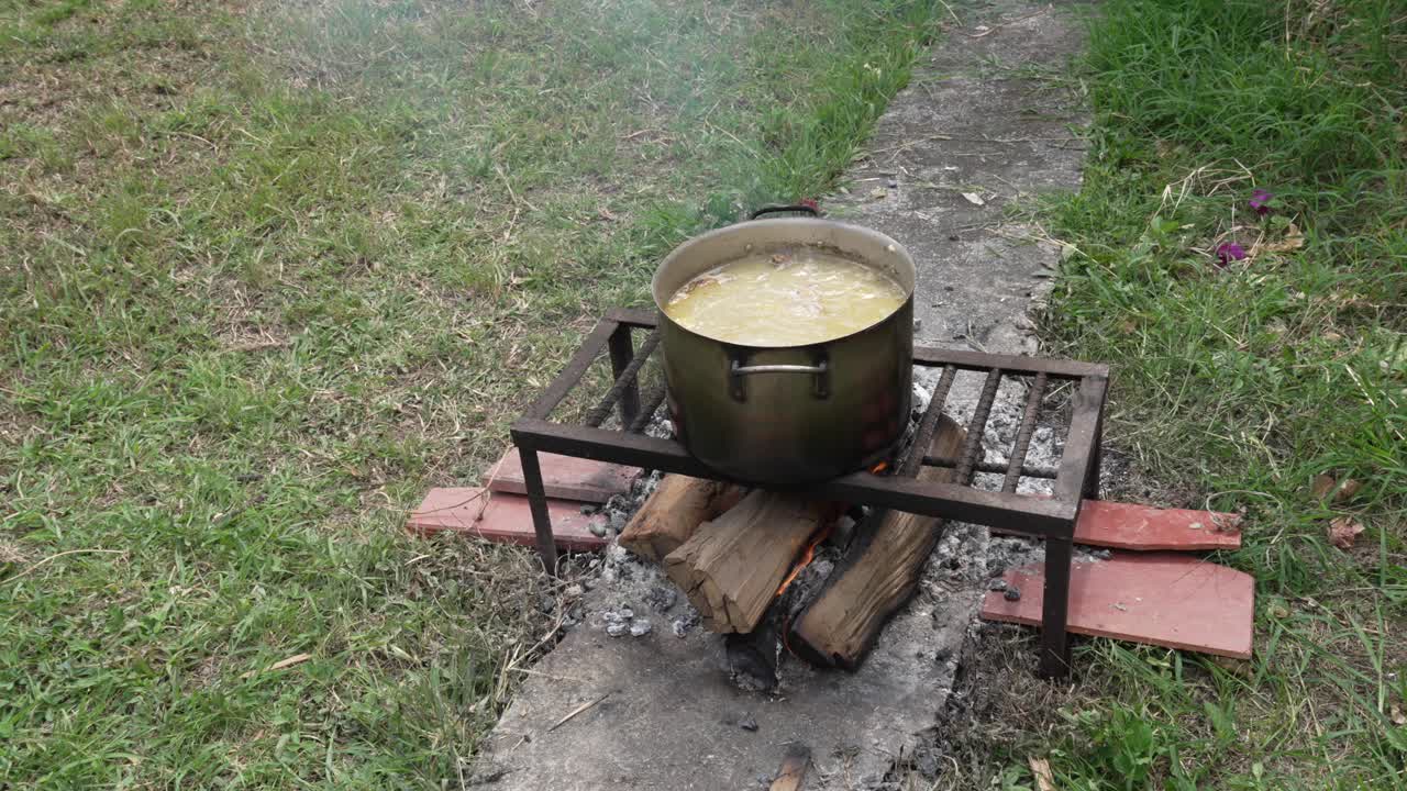Eye-level view of a large pot of stew boiling over a wood fire in a small village in Cachipay, Colombia. Green surroundings framing the rustic outdoor cooking scene