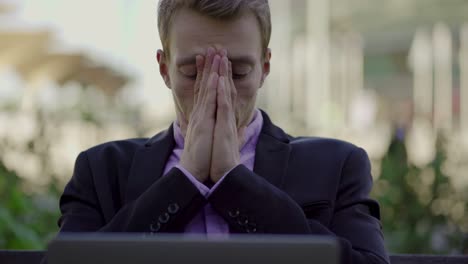 tired businessman taking off glasses and looking at laptop