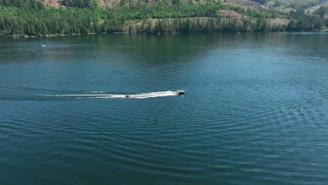 Toma-De-Drone-De-Una-Lancha-Arrastrando-A-La-Gente-Detrás-De-Ella-En-Spirit-Lake,-Idaho