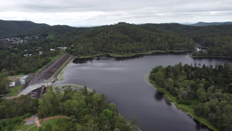 4k aerial drone shot of a water reservoir in australia with green bushland around and a concrete dam wall