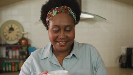 african american senior woman smiling while drinking coffee in the kitchen at home
