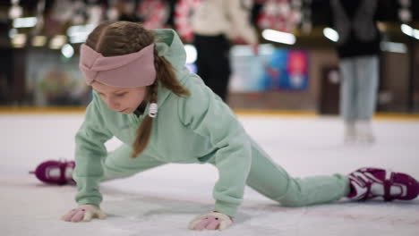 primer plano de una mujer patinando en una pista de hielo con patines púrpuras y traje verde menta, usando su mano en el hielo para el equilibrio, otros patinadores son visibles en el fondo