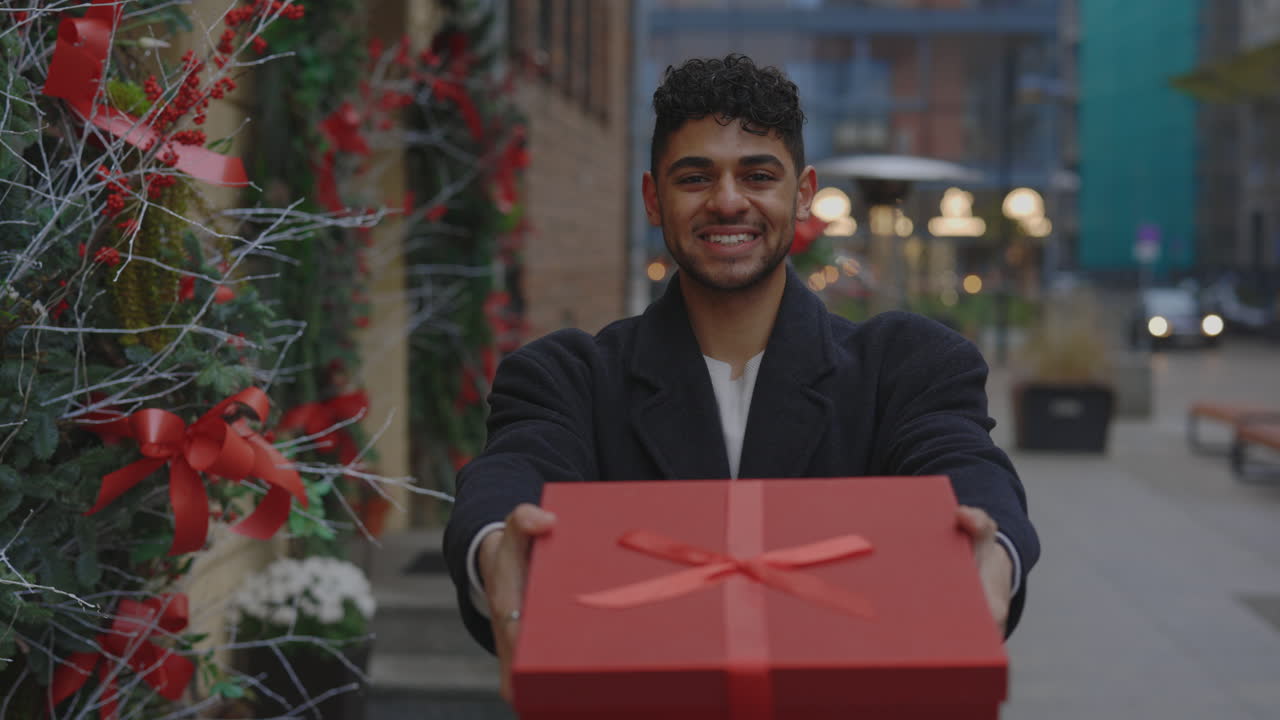 A smiling man offers a red Christmas gift box