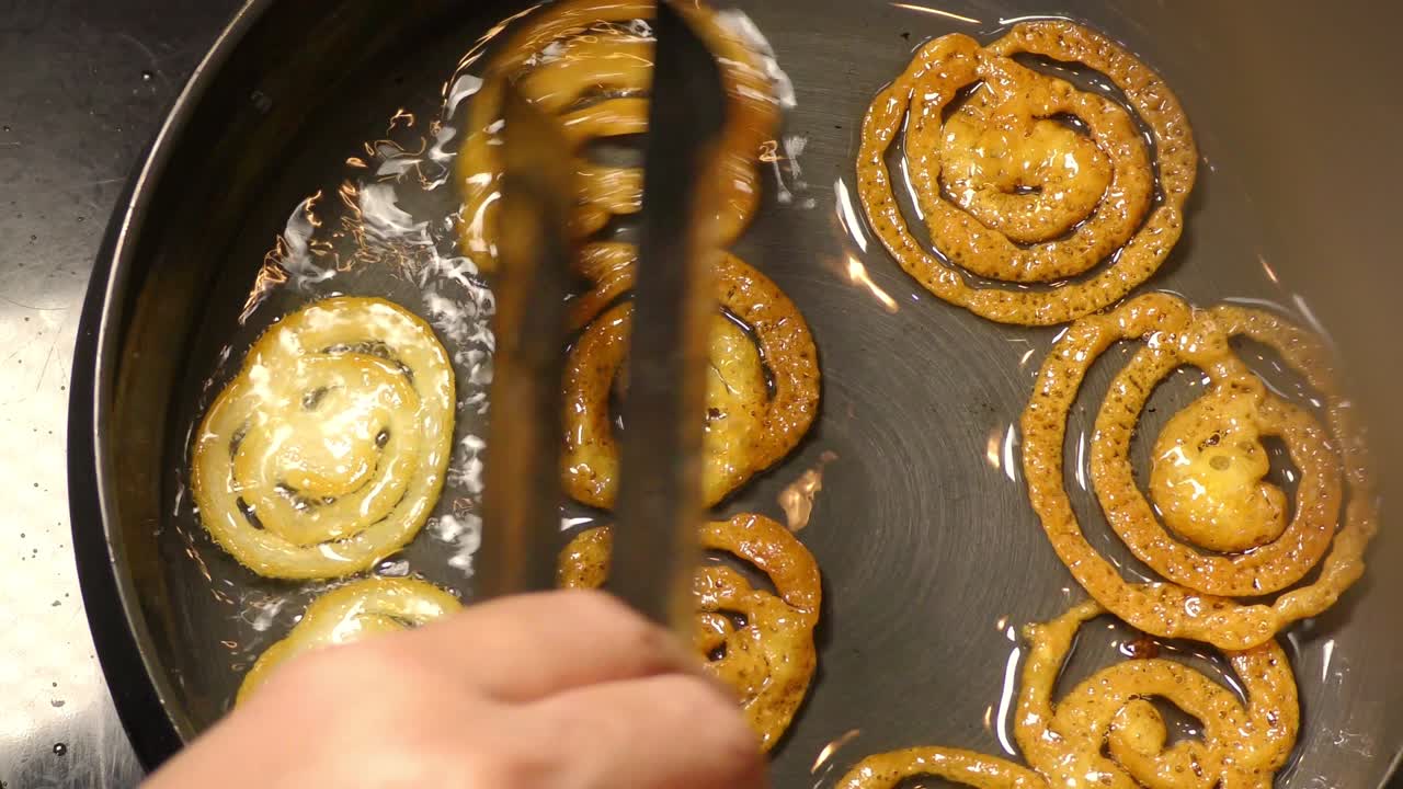 Frying jalebi brown and turning them in oil in heated pan