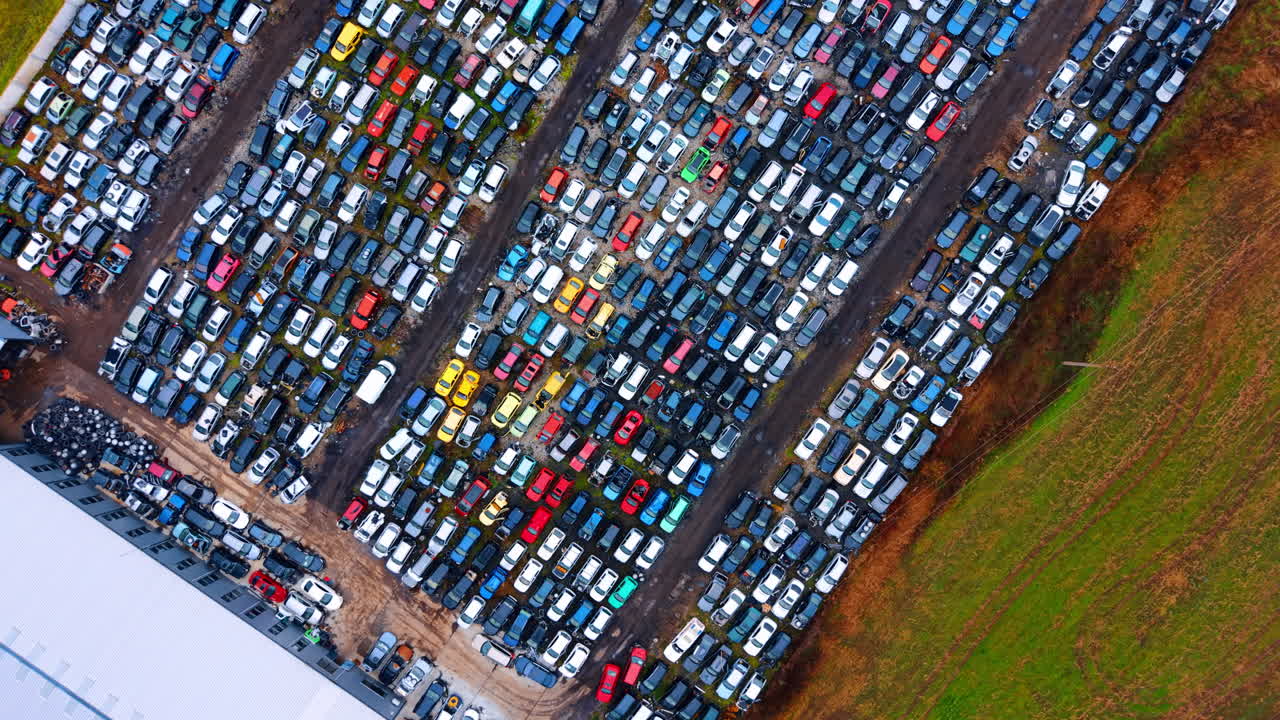 High angle view of extensive car junkyard near field. Wide aerial perspective of hundreds of scrapped vehicles arranged in rows next to a grassy area