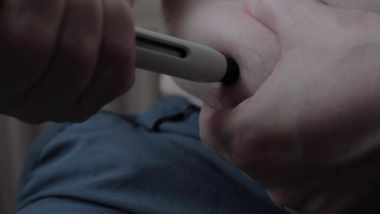 Close up of self applying of medicine through a medical needle pen injecting the substance in a fatty area of the abdomen leaving a mark of a drop of blood