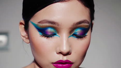 close-up of a woman showcasing vibrant and artistic eye makeup with bold pink lips