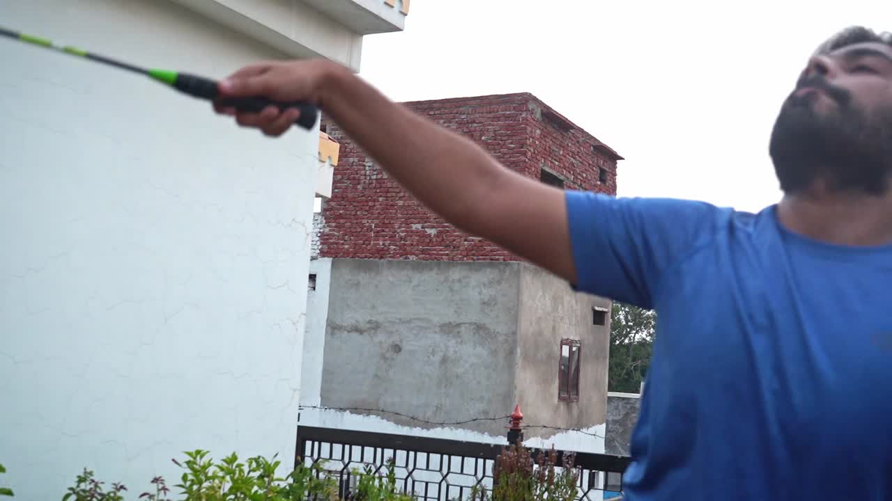 En skægget mand nyder at spille badminton i baghaven på en solrig morgen i Agra, Indien - Halvnært billede