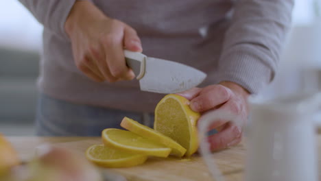 closeup of male hands cutting juicy lemon on wooden board.