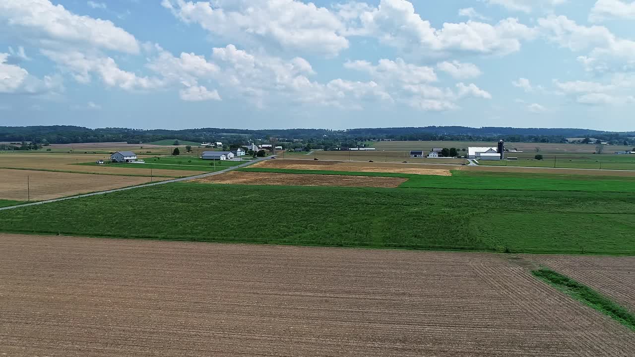 Eine langsame Luftaufnahme von Ackerland mit grünen und gepflügten Feldern an einem teils sonnigen Tag.