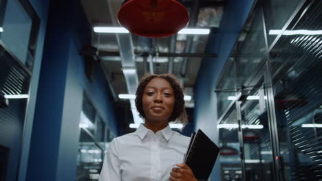 smiling afro woman waving hand in corridor. friendly businesswoman saying hi