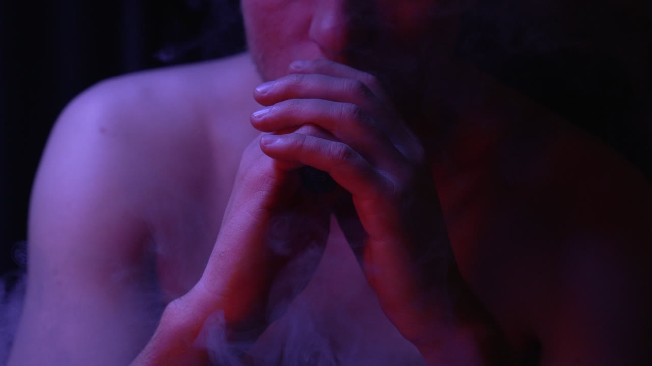 벌거 벗은 신비한 개인은 양손으로 vape를 피운다.