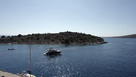 Drone-video-over-the-turquoise-waters-of-the-Albanian-coast-in-Porto-Palermo,-in-the-marina-in-front-of-the-island-of-Porto-Palermo,-passing-yachts-and-boats