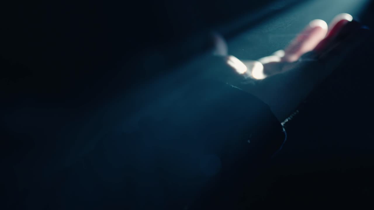 A hand reaches out to touch a concentrated beam of light in a pitch-black setting. The illumination highlights the contours of the fingers as they interact with the glowing ray