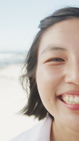 vertical video of portrait of happy asian woman smiling at beach, in slow motion