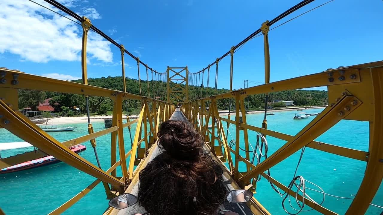 un ciclista conduce un scooter en un puente en nusa lembongan, indonesia - pov