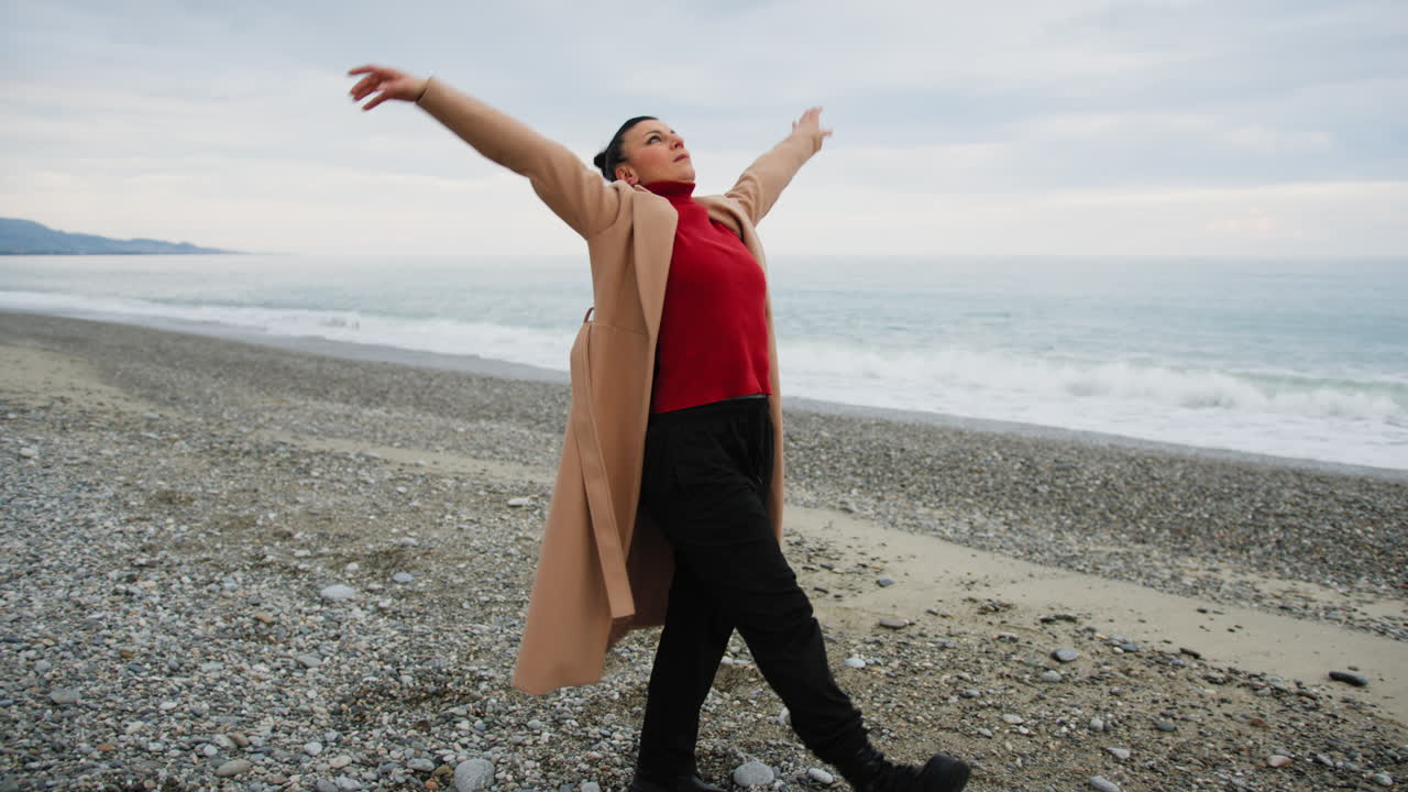 Sad Woman Dances With Long Brown Coat On Beach Near Ocean In Winter