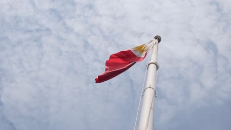 philippine national flag flying to the left filmed from under as the camera zooms out revealing cotton-like clouds