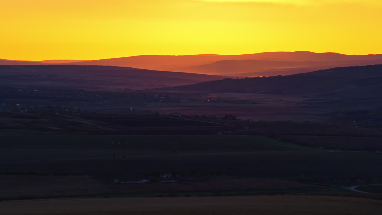 Aerial drone view of Moldova's rolling hills at dusk, layered in soft light with a glowing yellow orange sky