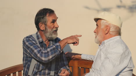 Close-Up-Of-The-Two-Old-Retired-Men-Neighbors-Disputing-While-Sitting-And-Resting-On-The-Bench-On-A-Sun