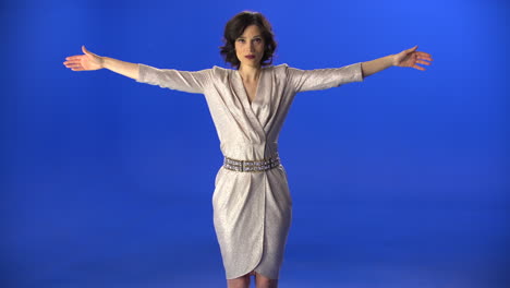 beautiful woman in a dress spreads her arms on a blue background in the studio