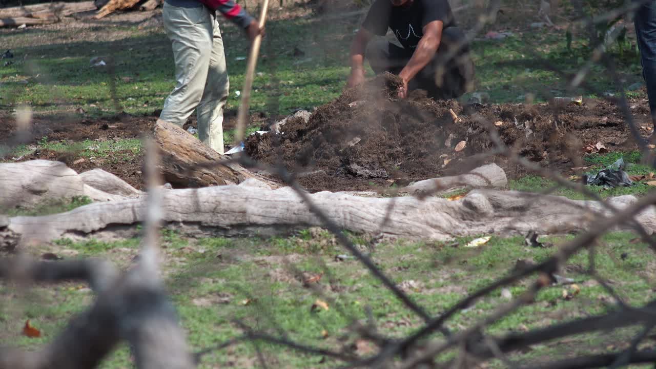 Medium Exterior Static Shot of Two Men Collect Dirt Into a Sack in the Day