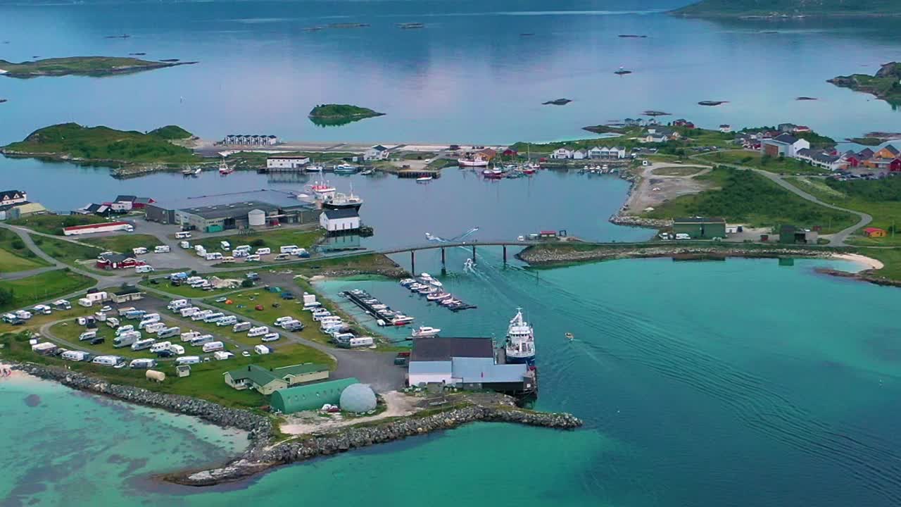 Aerial view overlooking boats heading towards the harbor at the Sommaroy village, at the Arctic ocean, cloudy, summer day, in Troms Nordland, Norway - orbit, drone shot