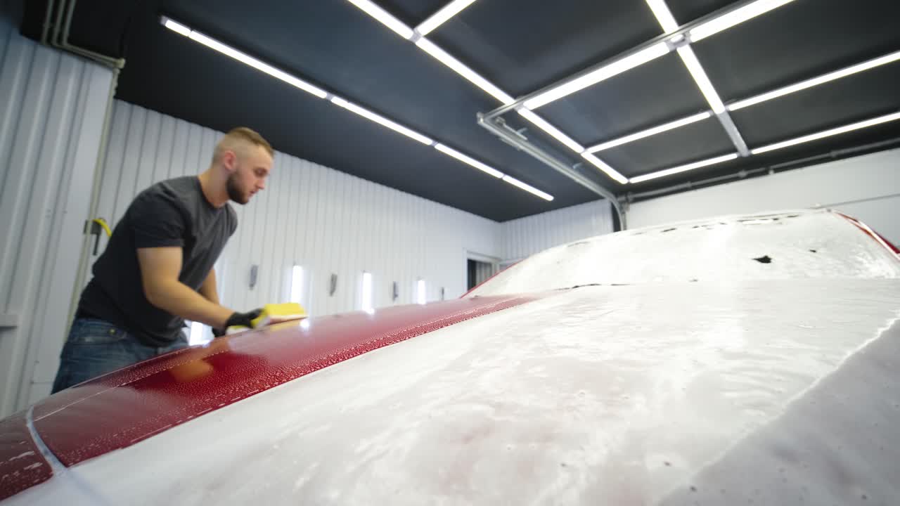 남성 노동자가 노란색 세탁구로 세탁장에서 빨간색 차를 고 있다.