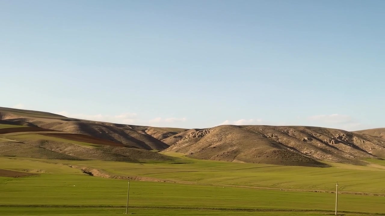 Naturskønt grønt bjergdalslandskab med panoramisk blå himmelbaggrund og traditionelle landsbyboere i hvedemarkens høstsæson, hvor husdyr græsser frodigt på en sommerhøjlandseng i Italien.