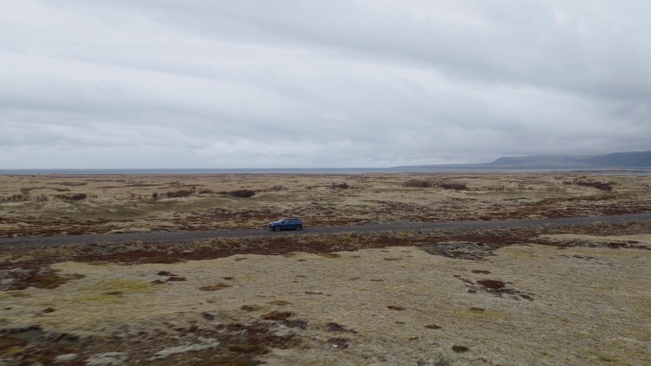 Lava field, Southwest Iceland, Iceland, revealing a four-wheel drive vehicle travelling along a gravel track across moss-covered basalt, volcanic plains and rugged lava terrain beneath overcast skies,